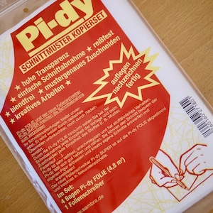 Op de afbeelding: Een pakket Pi-dy Schnittmuster Kopierset, een patroonkopieerset. De rood-witte verpakking bevat Duitse tekst, waaronder "hohe Transparenz" en "einfache Schnittabnahme". De set bevat 4 vellen Pi-dy folie en een foliepen.