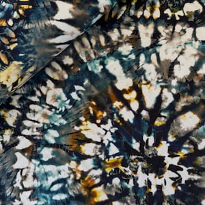 May include: A close-up shot of a fabric with a tie-dye design. The fabric displays a mix of colours, including navy blue, white, brown, and yellow. The pattern has a swirling, organic look, with the colours blending and overlapping to create a unique visual texture.