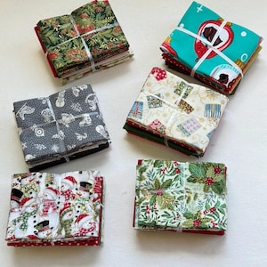 Puede incluir: Montones de cuadrados de tela con temática navideña, cada uno atado con hilo blanco. Las telas presentan varios patrones festivos, incluyendo muñecos de nieve, acebo, regalos y adornos. Los colores incluyen rojo, verde, blanco y gris.