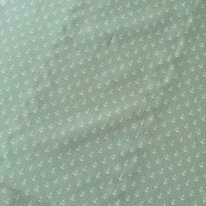 May include: A pale green fabric featuring a repeating pattern of small white anchors. The anchors are uniformly distributed across the material, creating a nautical theme. The fabric has a slightly textured appearance.
