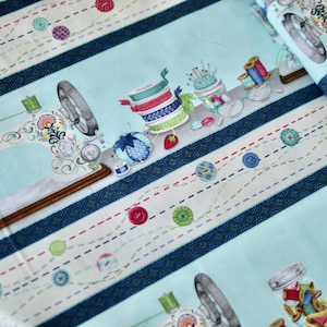 May include: A blue and white fabric with a repeating pattern of sewing machines, spools of thread, buttons, and needles. The fabric has a striped design with a blue, white, and red colour scheme.