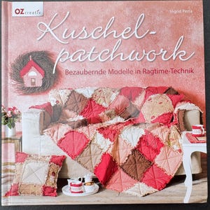 Könnte beinhalten: Ein gebundenes Buch mit dem Titel Kuschel-patchwork Bezaubernde Modelle in Ragtime-Technik von Ingrid Perra. Das Cover zeigt ein Foto eines Sofas, das mit einem rot, rosa und braun karierten Patchwork-Quilt, einem Kissen und einem Kranz bedeckt ist.