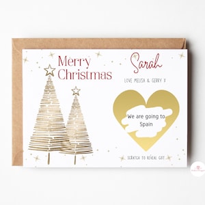 May include: A white Christmas card with a gold glitter design. The card features two gold glitter Christmas trees and a gold heart with a scratch-off area that reveals the text "We are going to Spain". The card is addressed to "Sarah" with the message "Love Melisa & Gerry X".