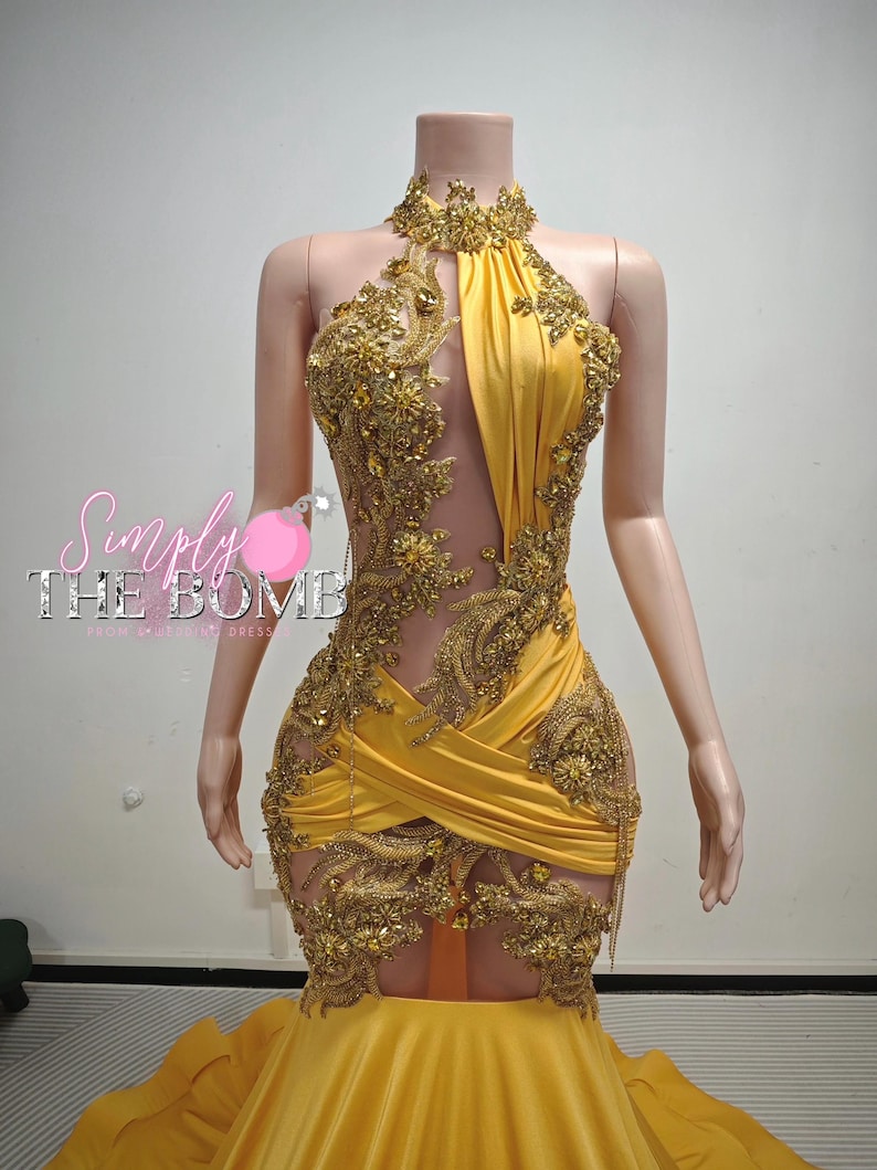 May include: A yellow halter-neck dress with gold embellishments and a sheer panel. The dress features intricate gold embroidery and a mermaid-style skirt. The dress is displayed on a mannequin.