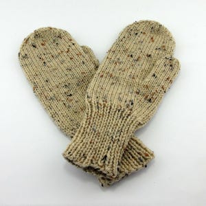 May include: A pair of beige knitted mittens with flecks of brown, black, and gray throughout the yarn. The mittens have ribbed cuffs and are displayed on a white background. The mittens are designed for warmth and comfort.