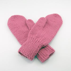 May include: A pair of pink knitted mittens. The mittens are made of a soft, textured yarn and feature a ribbed cuff. The mittens are designed to keep hands warm in cold weather. The mittens are a solid pink color.