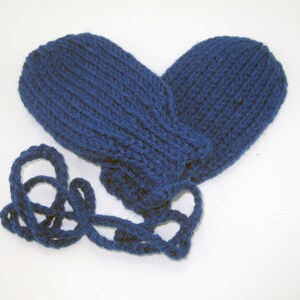 May include: A pair of navy blue knitted mittens connected by a matching cord. The mittens are made of a thick, textured yarn and are designed to keep hands warm. The cord allows the mittens to be worn together or hung up.