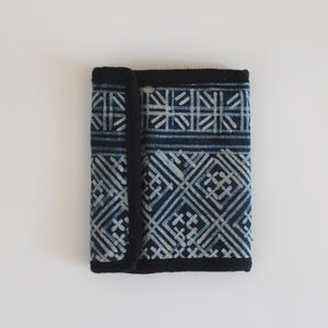 May include: A small, blue and white patterned wallet with a black border. The wallet is folded closed.