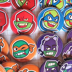 May include: A collection of 12 round pinback buttons featuring different Teenage Mutant Ninja Turtles characters. The buttons are colorful and feature various expressions and poses of the characters.
