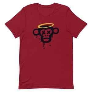 Puede incluir: Camiseta roja de manga corta con un gráfico negro y amarillo de un mono con un halo de ángel y X para los ojos.