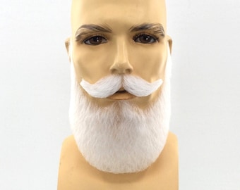 May include: A beige mannequin head featuring a thick, white synthetic beard and a matching handlebar mustache. The facial hair is styled with a full, rounded beard covering the chin and jawline, paired with a curled, upward-swept mustache.