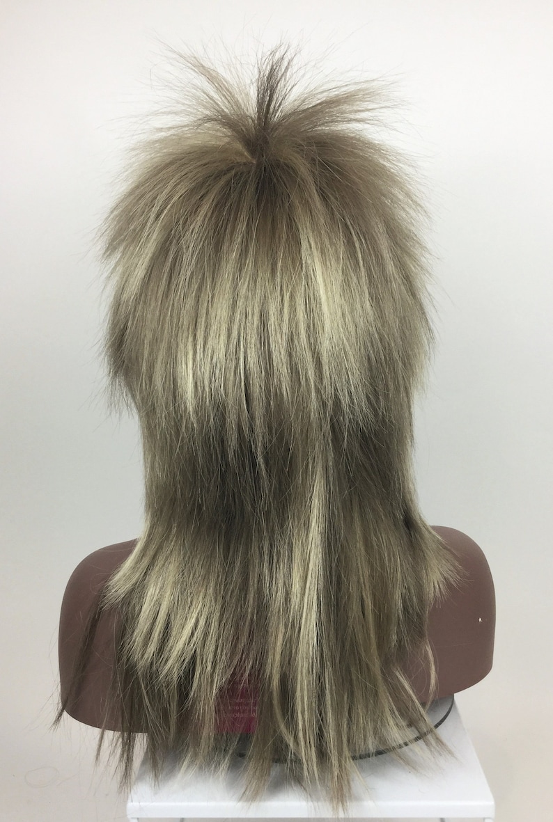 Op de afbeelding: Een lange, gelaagde pruik in een lichtbruine en blonde kleur. De pruik is gestyled met een middenscheiding en heeft een ruige, textuurrijke look.