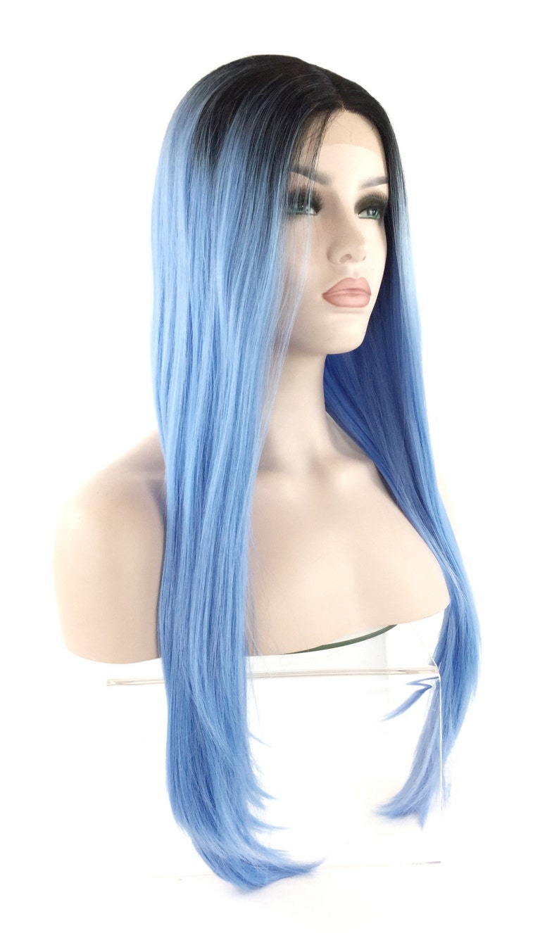 May include: A long, straight wig with a black to light blue ombre effect. The wig is styled on a mannequin head, showcasing the color transition from dark roots to a vibrant blue. The hair appears smooth and sleek, with a natural-looking hairline.