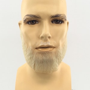 May include: A mannequin head with a realistic appearance. The head has brown eyes, eyebrows, and a light blonde beard. The skin tone is a pale beige color. The mannequin is designed for displaying hats, wigs, or other accessories.