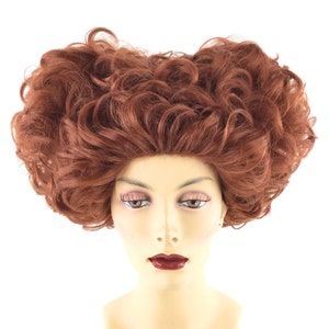 May include: A red curly wig with a large, voluminous style. The wig is on a mannequin head.