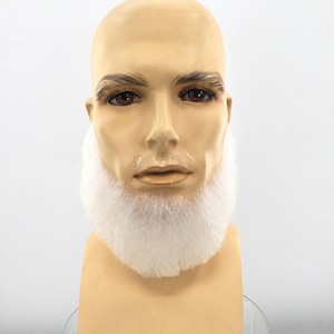 Peut inclure: Une tête de mannequin beige dotée d'une barbe synthétique blanche, épaisse et fournie. Le mannequin présente des traits faciaux moulés, notamment des yeux marron et des sourcils foncés, avec la barbe blanche fixée au menton et à la mâchoire.