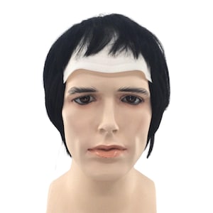 May include: A mannequin head with a black wig and a white strip across the forehead. The wig has short, straight bangs and is styled with a slight side part. The mannequin has realistic facial features.