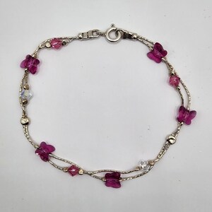 May include: A silver chain bracelet with two strands of delicate chain. The bracelet is adorned with small pink butterfly charms and clear crystal accents.