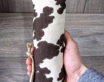 May include: A brown and white cow print fabric dog toy with a knotted rope handle.