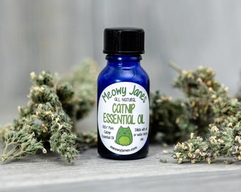 May include: A blue glass bottle with a black cap and a white label that reads "Meowy Janes All Natural Catnip Essential Oil". The label also features a cartoon cat and the text "100% Pure Catnip Essential Oil" and "Dilute with oil or water before use".