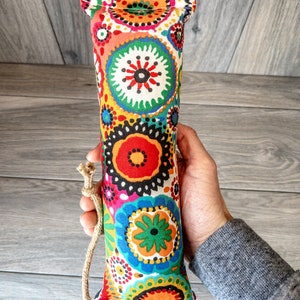 May include: A colorful, cylindrical dog toy with a floral pattern. The toy is made of fabric and has a rope attached to one end.