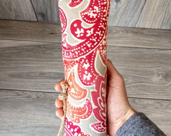 Puede incluir: Un tapón de puerta de tela con estampado rojo, naranja y blanco con un asa de cuerda marrón.