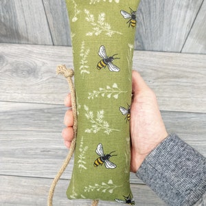May include: A green fabric pouch with a drawstring closure. The pouch is decorated with a repeating pattern of white flowers and yellow and black bees.