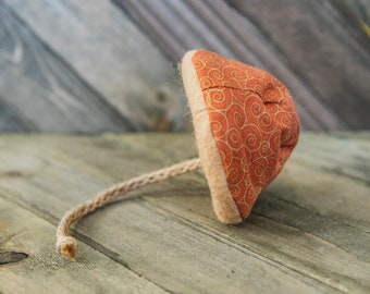 May include: A brown and orange fabric toy with a long, thin rope attached. The fabric has a swirl pattern.