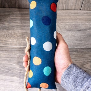 May include: A blue fabric toy with colorful polka dots and a brown rope tied around it. The toy is being held in a hand.