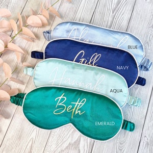 May include: Four satin sleep masks in different colors with white piping and personalized names in gold lettering. The colors are blue, navy, aqua, and emerald.