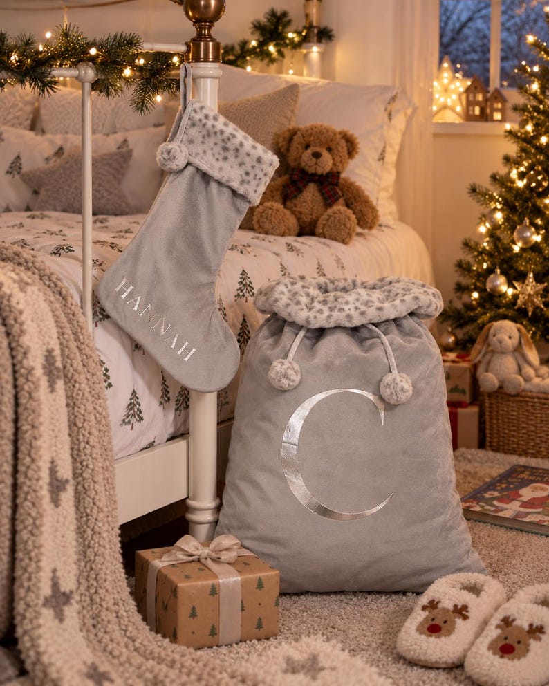 May include: A gray velvet Christmas stocking with the name HANNAH embroidered in white and a gray velvet Santa sack featuring a large silver letter C, both trimmed with a white and gray leopard print faux fur cuff and matching pom-poms.