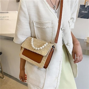 May include: A brown and beige woven straw handbag with a brown leather flap and a pearl chain strap.