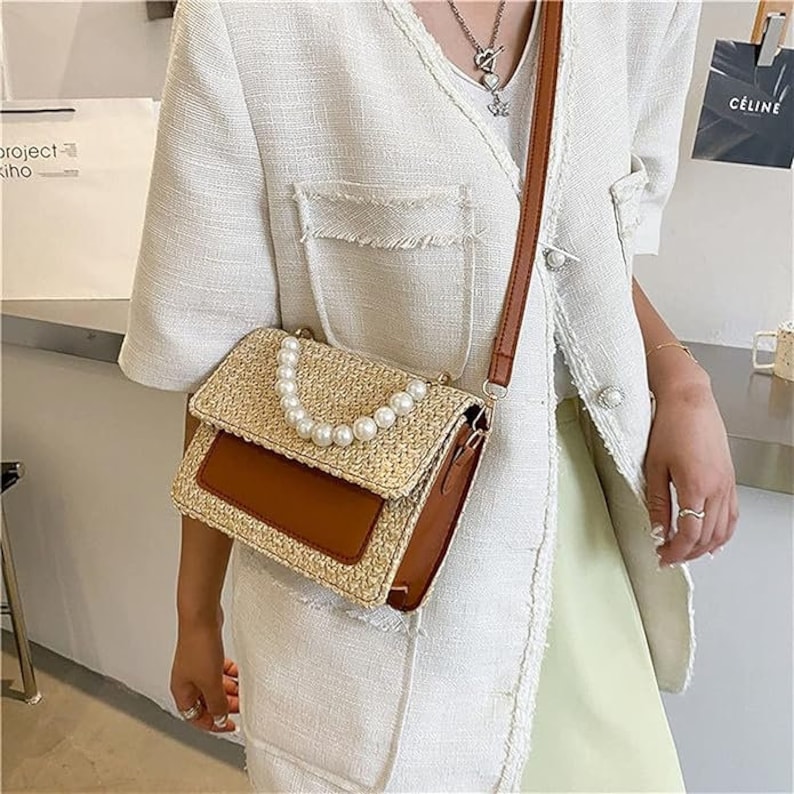 May include: A brown and beige woven straw handbag with a brown leather flap and a pearl chain strap.