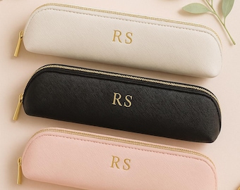 May include: Three rectangular pencil cases in cream, black, and light pink, each featuring a gold zipper and the gold embossed letters RS centered on the front. The cases have a textured finish and are arranged horizontally in a stack.