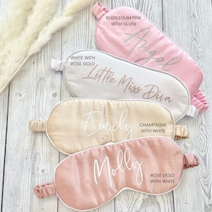May include: Four satin sleep masks with different colors and personalized names. The masks are white with rose gold lettering, champagne with white lettering, bubblegum pink with silver lettering, and rose gold with white lettering.