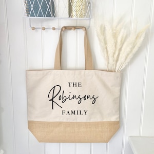 May include: A beige canvas tote bag with a jute bottom. The bag has black text that reads "THE Robinsons FAMILY".