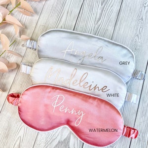 May include: Three satin sleep masks in different colors: grey, white, and watermelon. Each mask has a different name embroidered on it in gold lettering: Angela, Madeleine, and Penny.