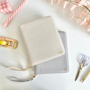 May include: Two zippered leather planners with gold handles and gold initials. The top planner is cream colored with the initials "AW" and the bottom planner is gray with the initials "JR".