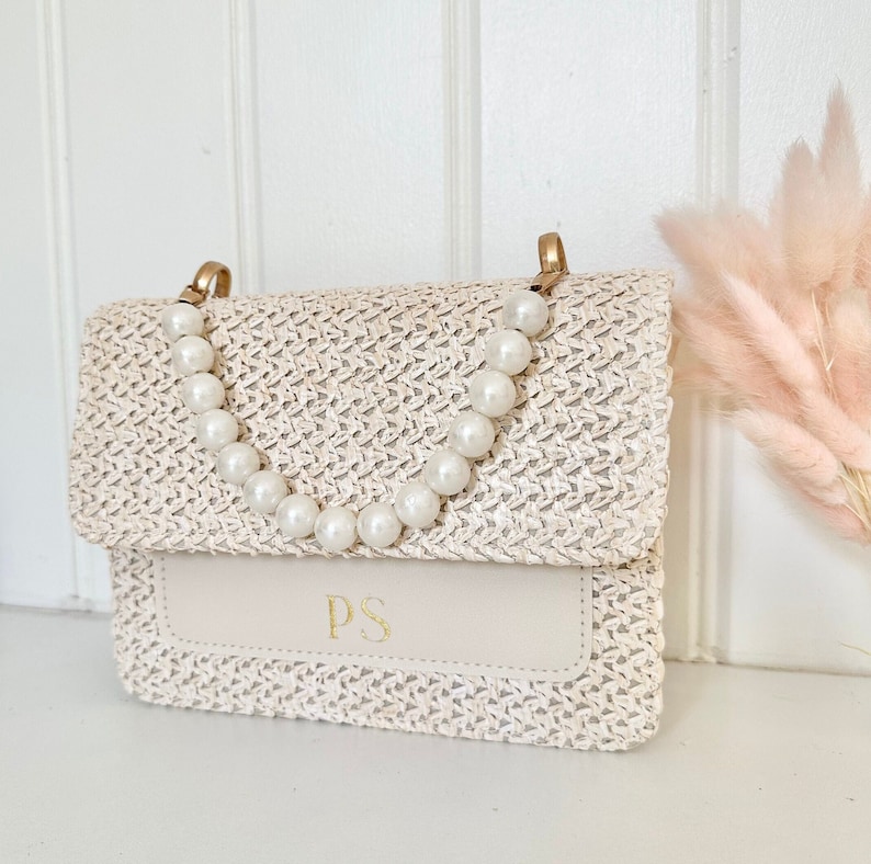 May include: A white woven straw handbag with a pearl chain strap and a cream leather flap with the initials "PS" in gold lettering.