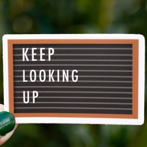 Peut inclure: Un tableau d'affichage noir avec un cadre brun et des lettres blanches qui épellent "KEEP LOOKING UP".