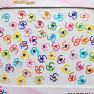 May include: A sheet of colorful Om symbol stickers with rhinestones. The stickers are arranged in rows on a white background. The sheet is labeled "The Designers" and "Made in India".
