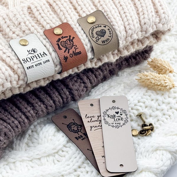 May include: Rectangular faux leather labels in white, tan, and brown with gold-tone metal rivets. The labels feature custom text and graphics including "SOPHIA", "Knit with Love", "Handmade With Love", and "Knit with Love by Diane" with yarn motifs.