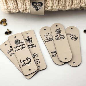 Puede incluir: Etiquetas rectangulares de piel sint&eacute;tica beige con extremos redondeados, con texto e iconos impresos en negro que incluyen ovillos de lana, corazones y nombres como Nana Steph y Aunt Mary. Incluye remaches de metal bronce.