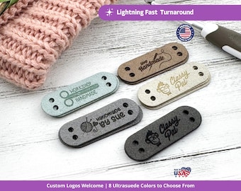 May include: A collection of ultrasuede labels in various colors, each with a unique logo and text, including "Workshop Handmade," "Handmade by Sue," and "Classy Pal." The labels are designed for handmade crafts and feature pre-drilled holes for easy attachment.