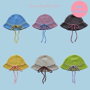 May include: Six crocheted bucket hats with different colored brims and matching ribbon ties. The hats are arranged in two rows of three. The hats are all the same style, but each has a different color combination. The hats are all made with a crochet stitch. The hats are all in focus. The background is a light blue color. The text "bow bucket hat" is at the top of the image. The text "PDF Pattern" is in a pink circle at the top right of the image.