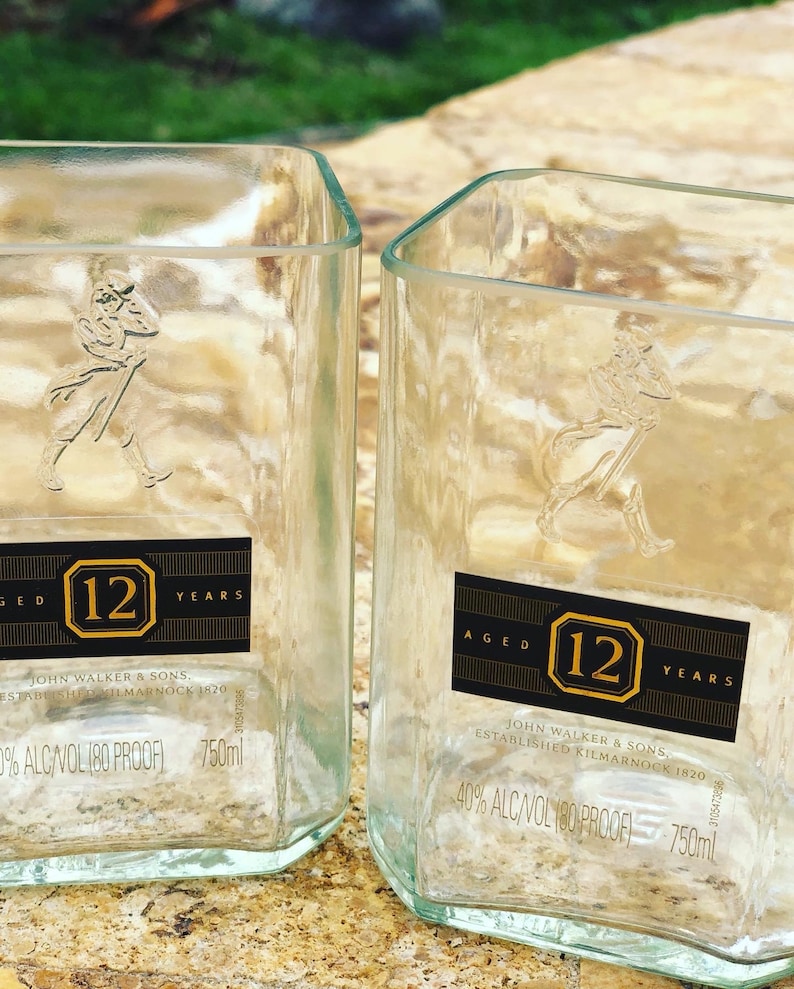 Op de afbeelding: Twee doorzichtige glazen flessen met een zwart etiket waarop "Aged 12 Years" en "John Walker & Sons. Established Kilmarnock 1820" staat. De flessen zijn 750 ml en hebben een alcoholpercentage van 40%.