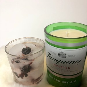 K&ouml;nnte beinhalten: Ein Glas Gin Tonic mit Eis und Brombeeren neben einer gr&uuml;nen Glasflasche Tanqueray London Dry Gin.