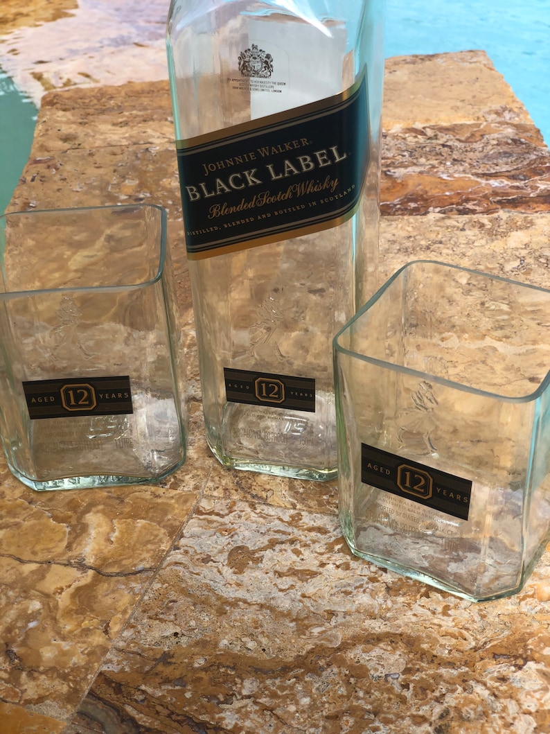 Op de afbeelding: Drie doorzichtige glazen flessen met een gouden etiket waarop "JOHNNIE WALKER. BLACK LABEL Blended Scotch Whisky" en "AGED 12 YEARS" staat.