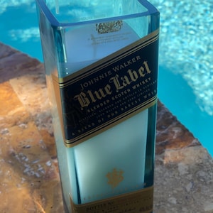 May include: A blue glass candle holder shaped like a Johnnie Walker Blue Label whiskey bottle. The label reads "Johnnie Walker Blue Label Blended Scotch Whisky" and "A blend of our rarest whiskies".