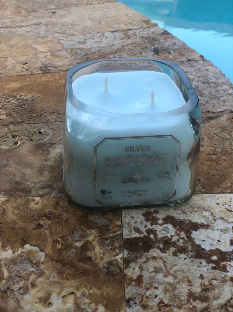 May include: A clear glass candle jar with a blue wax candle inside. The jar is labeled "SILVER PATR&Oacute;N" with the text "HECHO EN M&Eacute;XICO" and "TEQUILA, M&Eacute;XICO".
